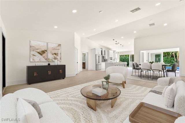 living room featuring lofted ceiling, sink, and light hardwood / wood-style flooring