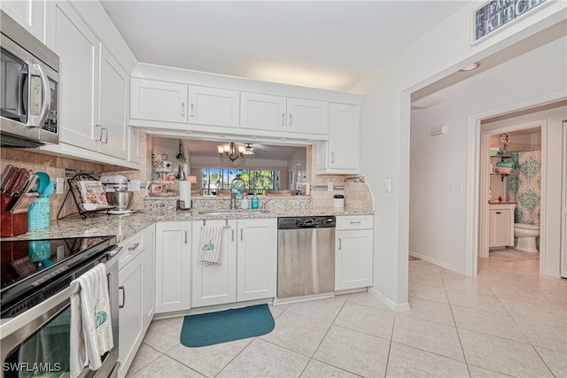 kitchen with sink, an inviting chandelier, stainless steel appliances, light stone countertops, and white cabinets