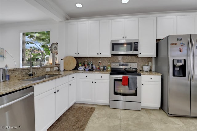 kitchen with white cabinets, appliances with stainless steel finishes, ornamental molding, and sink