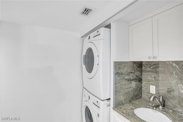laundry room with stacked washer and dryer, visible vents, and a sink