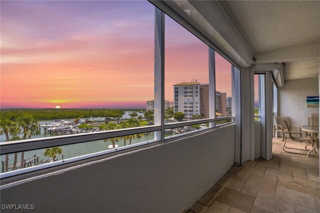 balcony at dusk featuring a water view