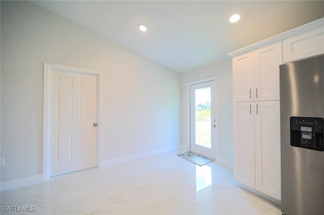 kitchen featuring stainless steel refrigerator with ice dispenser, vaulted ceiling, and white cabinetry