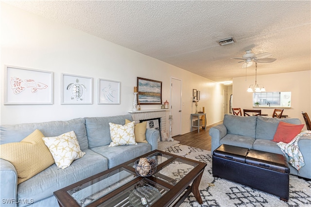 living room with hardwood / wood-style floors, ceiling fan with notable chandelier, a textured ceiling, and a brick fireplace