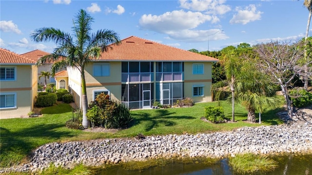 back of house featuring a water view, a lawn, and a tiled roof