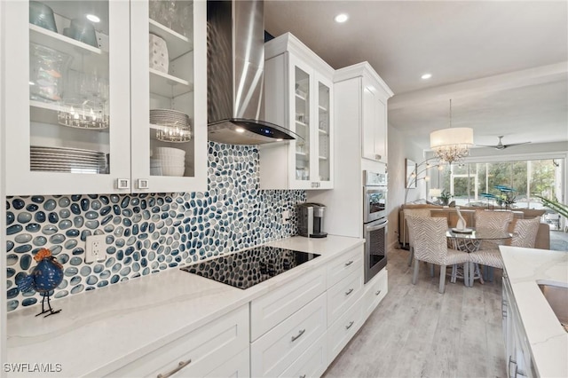 kitchen with black electric cooktop, white cabinets, light stone countertops, wall chimney exhaust hood, and glass insert cabinets