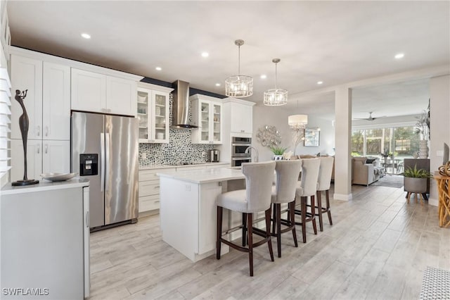 kitchen with glass insert cabinets, appliances with stainless steel finishes, light countertops, wall chimney range hood, and pendant lighting