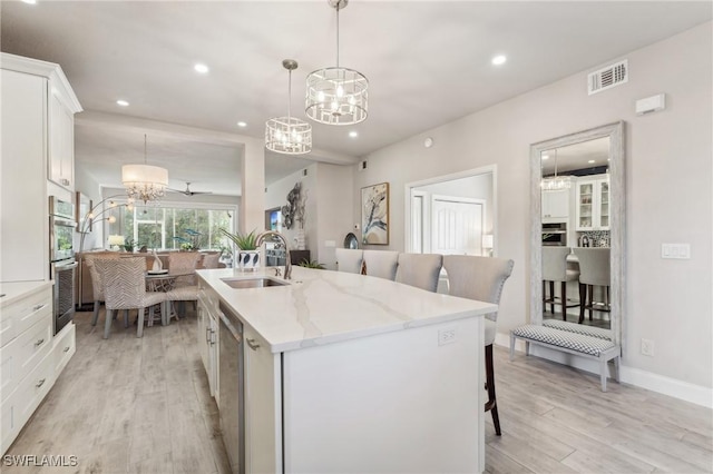 kitchen with a chandelier, a sink, white cabinets, an island with sink, and decorative light fixtures