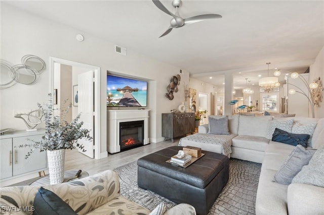 living room featuring light wood-style flooring, a glass covered fireplace, visible vents, and a ceiling fan