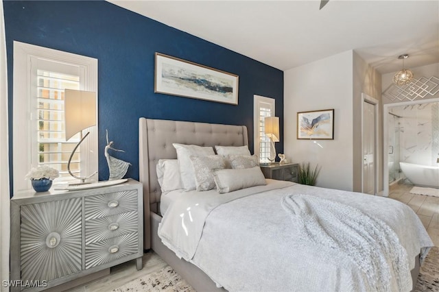 bedroom featuring a notable chandelier, ensuite bath, and light hardwood / wood-style flooring