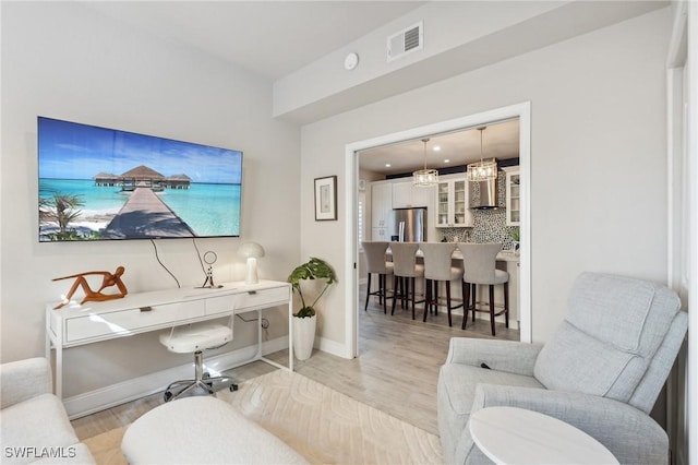 office area with visible vents, light wood-style flooring, baseboards, and an inviting chandelier