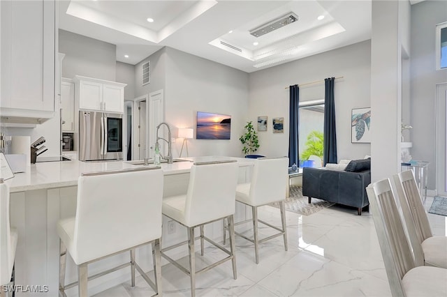 kitchen featuring stainless steel refrigerator, sink, a high ceiling, a kitchen breakfast bar, and white cabinets