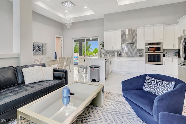 living room with a raised ceiling, a towering ceiling, sink, and an inviting chandelier