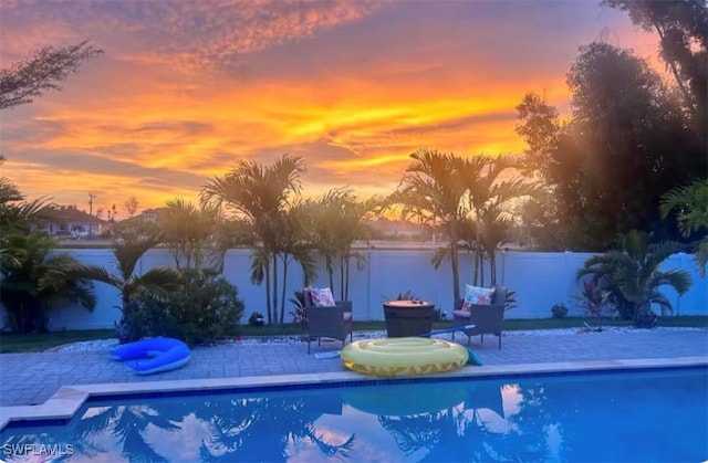 pool at dusk with a water view and a patio