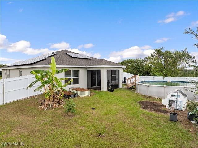 rear view of house featuring a sunroom, solar panels, a fenced in pool, and a lawn