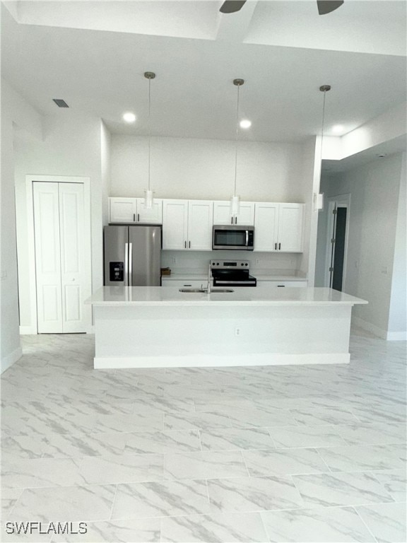 kitchen with appliances with stainless steel finishes, a center island with sink, white cabinetry, and pendant lighting