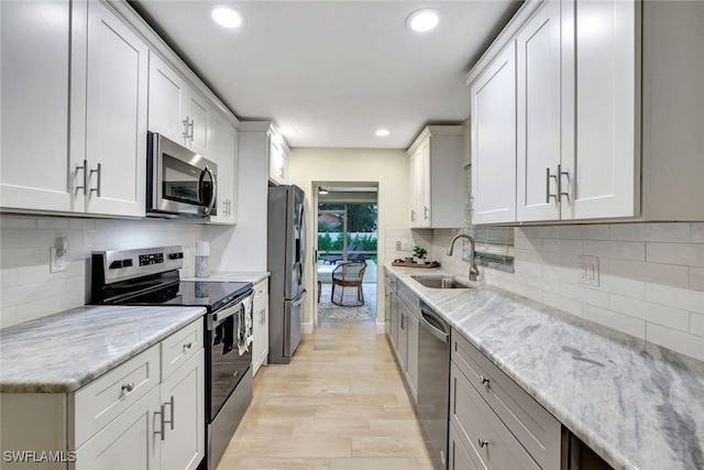 kitchen with white cabinetry, sink, stainless steel appliances, and light hardwood / wood-style flooring