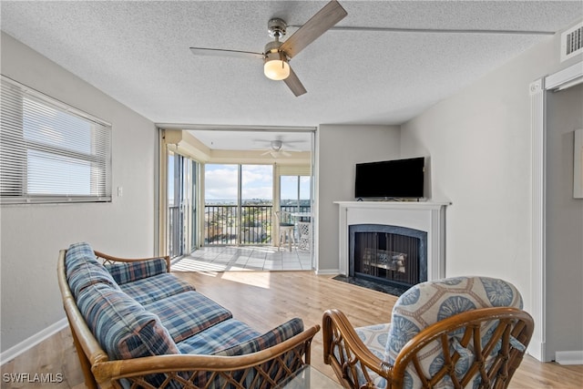 living room featuring ceiling fan, light hardwood / wood-style flooring, and a textured ceiling