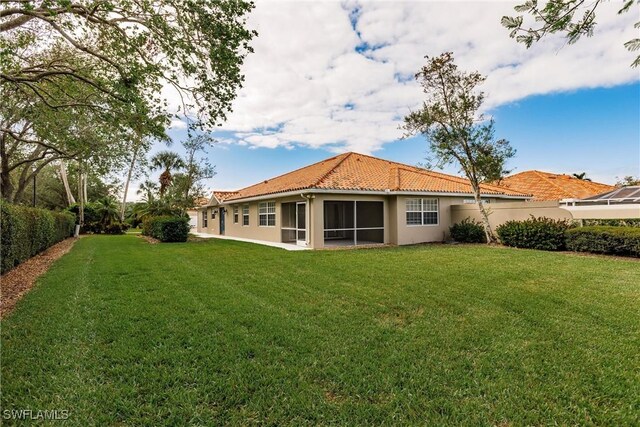 rear view of property featuring a sunroom, a tile roof, fence, a yard, and stucco siding