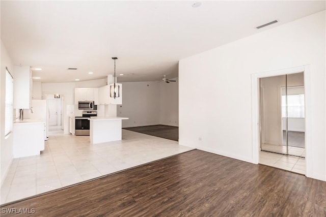 interior space featuring white cabinetry, pendant lighting, ceiling fan, stainless steel appliances, and light hardwood / wood-style floors