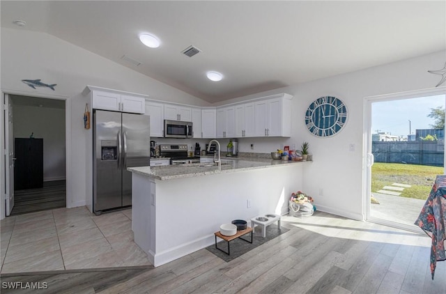 kitchen featuring appliances with stainless steel finishes, vaulted ceiling, light hardwood / wood-style floors, and white cabinetry