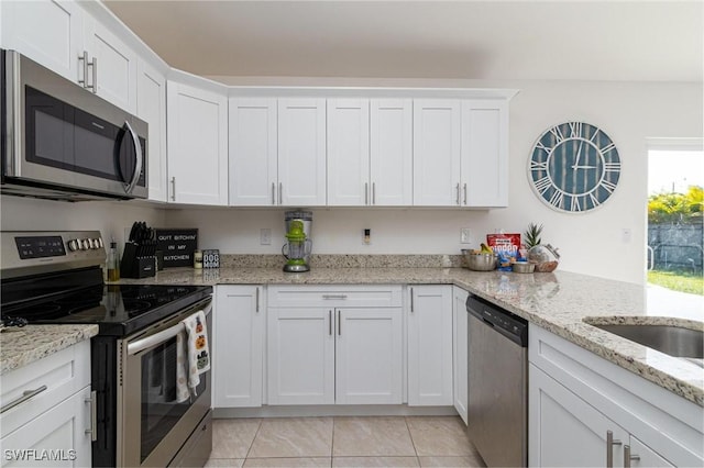 kitchen with light stone countertops, light tile patterned floors, stainless steel appliances, and white cabinetry