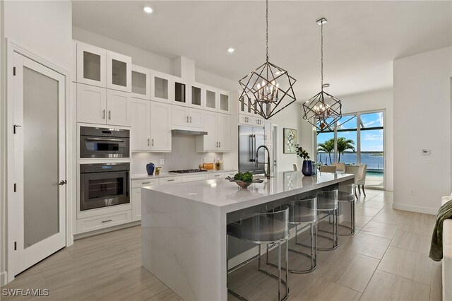 kitchen with sink, gas cooktop, a kitchen island with sink, a breakfast bar, and a water view