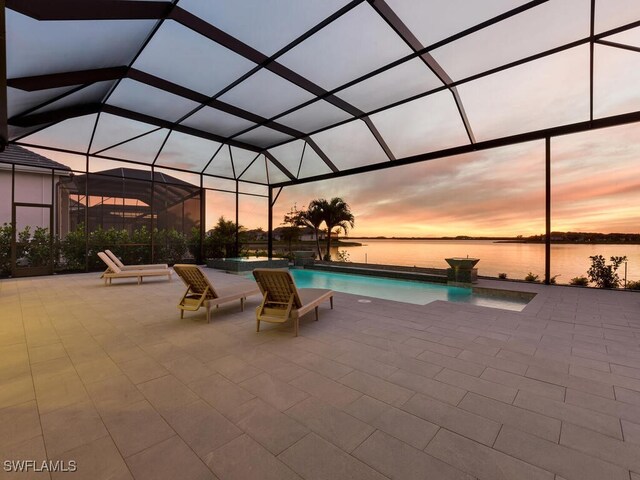 pool at dusk featuring glass enclosure, a water view, and a patio