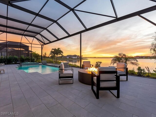 pool at dusk with an outdoor fire pit, a lanai, pool water feature, a patio area, and a water view