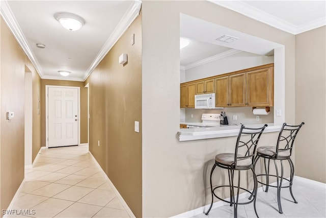 kitchen with light tile patterned floors, crown molding, white appliances, a breakfast bar area, and kitchen peninsula