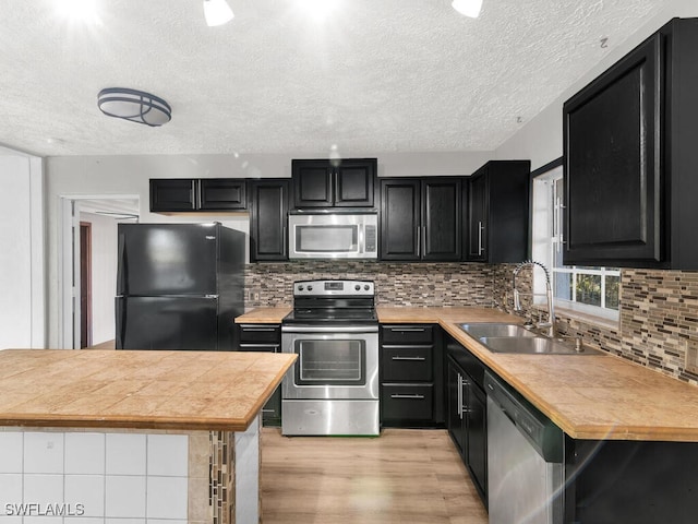 kitchen with sink, decorative backsplash, a textured ceiling, light hardwood / wood-style floors, and stainless steel appliances