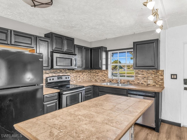 kitchen with appliances with stainless steel finishes, light wood-type flooring, backsplash, sink, and tile counters