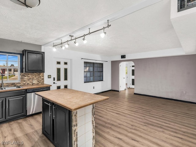 kitchen with stainless steel dishwasher, sink, tile countertops, light hardwood / wood-style flooring, and a center island