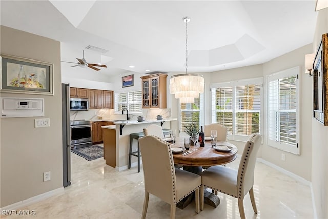 dining area featuring sink, a healthy amount of sunlight, ceiling fan with notable chandelier, and a tray ceiling