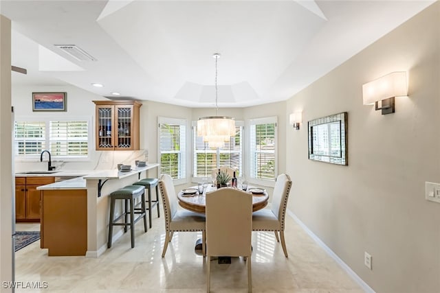 dining area featuring sink, a raised ceiling, and a notable chandelier