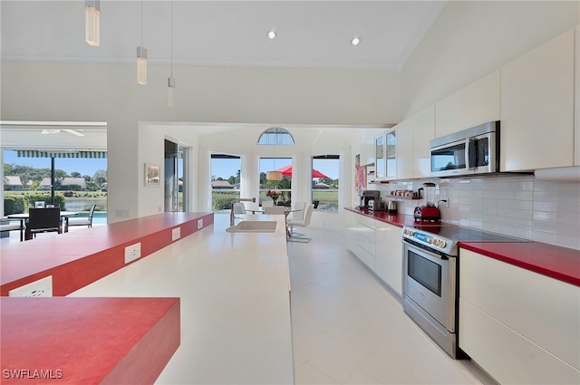 kitchen featuring decorative backsplash, appliances with stainless steel finishes, sink, white cabinetry, and hanging light fixtures