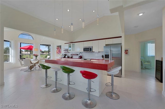 28450 Rochester Ct, Bonita Springs, FL 34135 - kitchen featuring appliances with stainless steel finishes, white cabinets, a kitchen bar, high vaulted ceiling, and plenty of natural light