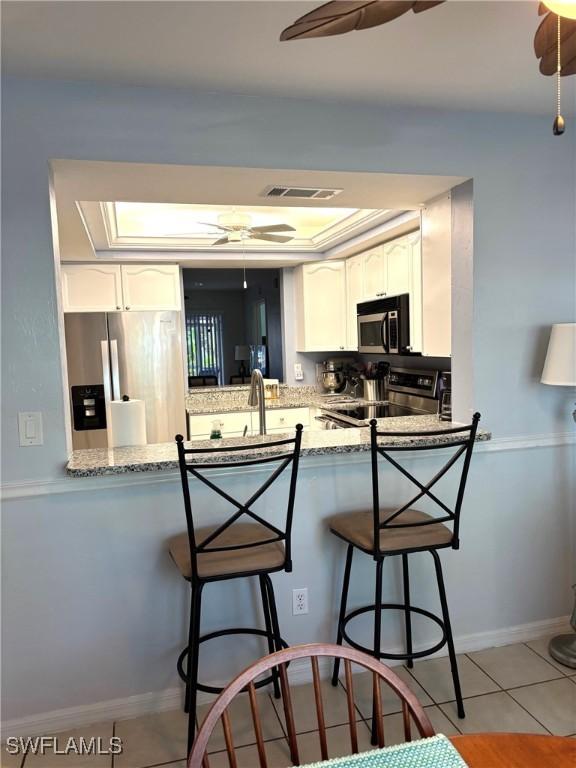 kitchen with white cabinets, a kitchen breakfast bar, ceiling fan, kitchen peninsula, and stainless steel appliances