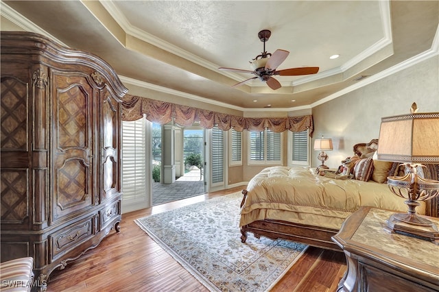 bedroom featuring ceiling fan, light hardwood / wood-style floors, a raised ceiling, and access to outside