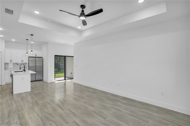 unfurnished living room with a tray ceiling, ceiling fan, light hardwood / wood-style floors, and sink