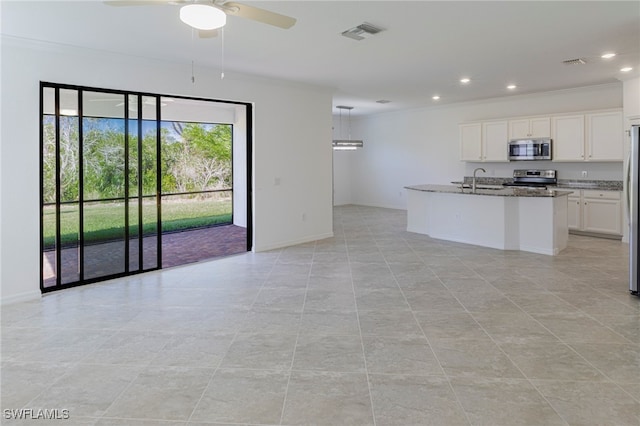 kitchen featuring ceiling fan, stainless steel appliances, dark stone countertops, a center island with sink, and white cabinets