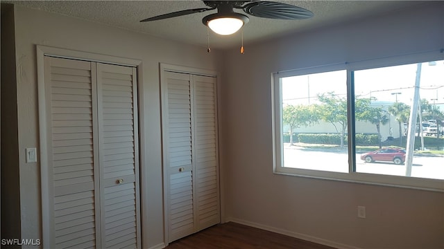 unfurnished bedroom featuring a textured ceiling, ceiling fan, dark hardwood / wood-style floors, and two closets