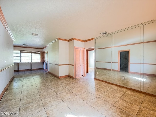 tiled empty room featuring a textured ceiling and ornamental molding