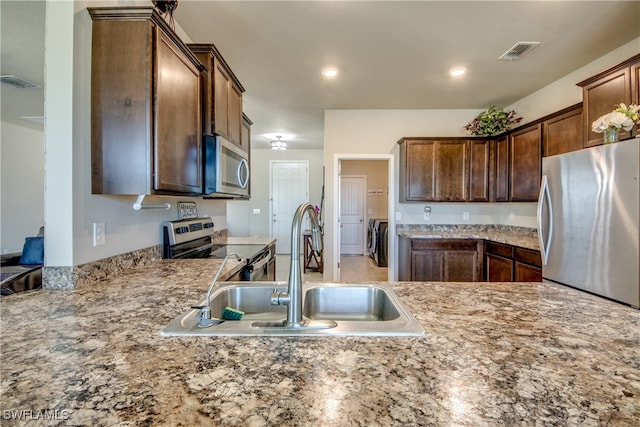 kitchen with light stone countertops, sink, separate washer and dryer, and stainless steel appliances