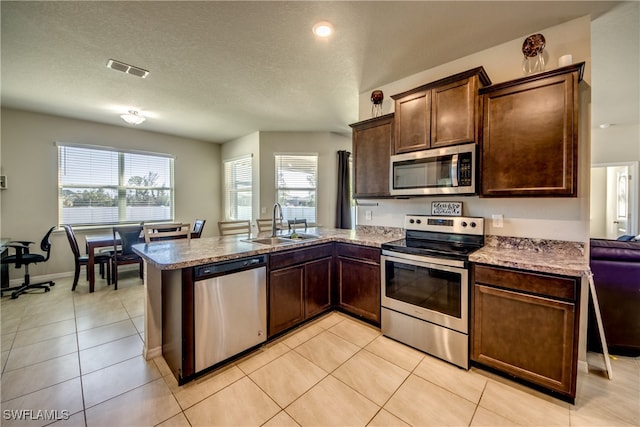 kitchen with sink, kitchen peninsula, a textured ceiling, light tile patterned floors, and appliances with stainless steel finishes