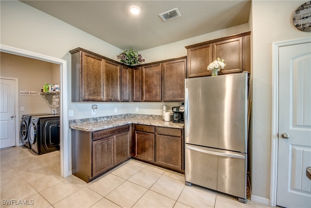 kitchen featuring light stone counters, dark brown cabinets, separate washer and dryer, stainless steel refrigerator, and light tile patterned flooring