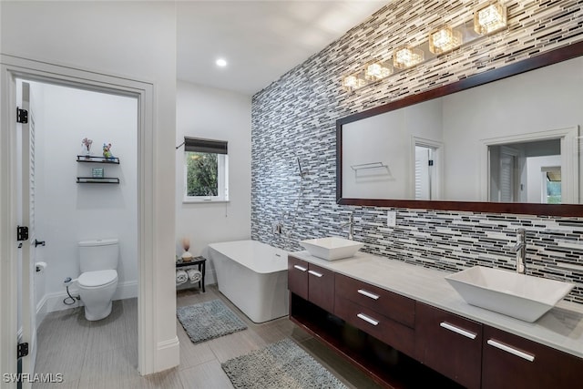 bathroom with vanity, tile patterned floors, toilet, a tub to relax in, and tasteful backsplash