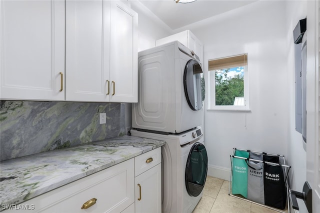 laundry room featuring cabinets, light tile patterned floors, and stacked washer / dryer