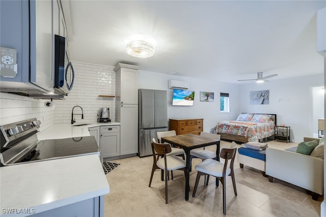 interior space with a wall mounted air conditioner, sink, decorative backsplash, ceiling fan, and stainless steel appliances