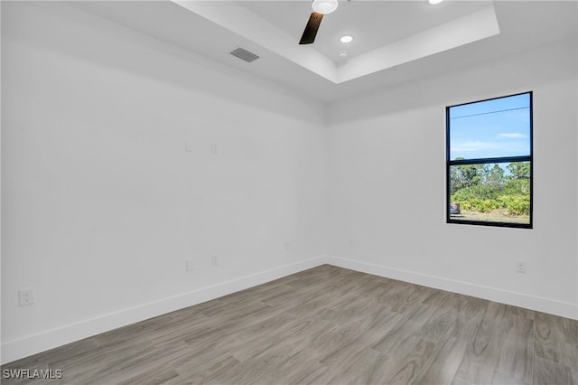 spare room featuring light wood-type flooring, a raised ceiling, and ceiling fan