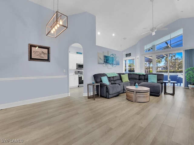 living room featuring ceiling fan with notable chandelier, light wood-type flooring, and high vaulted ceiling